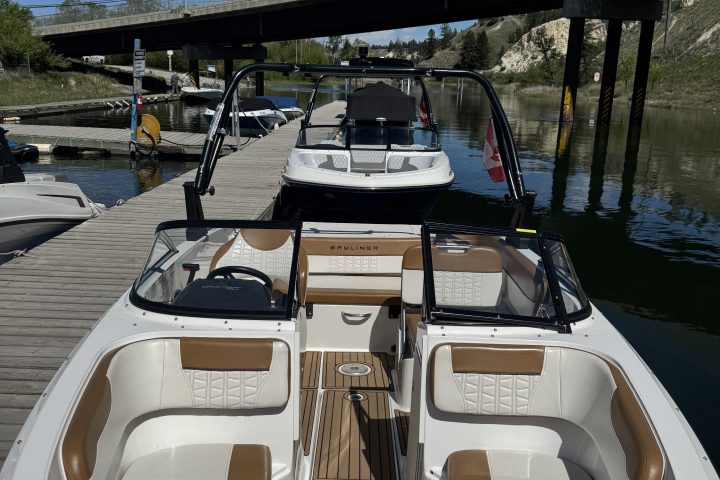 Two motorboats docked next to a wooden pier under a bridge.