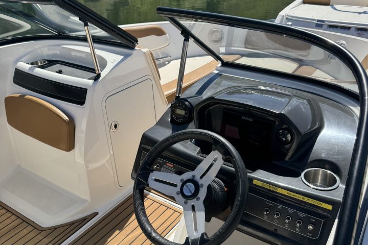 View of a boat's cockpit with steering wheel and control panel, docked on a calm water body.