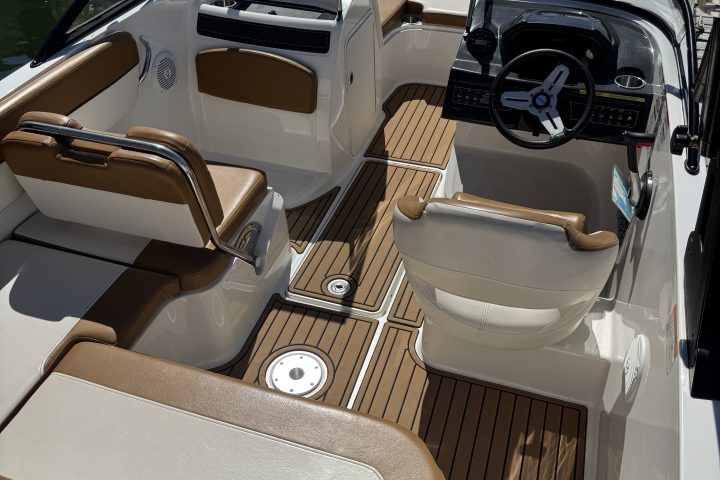 Interior of a boat with brown seats and wooden flooring, featuring a steering wheel and gauges.