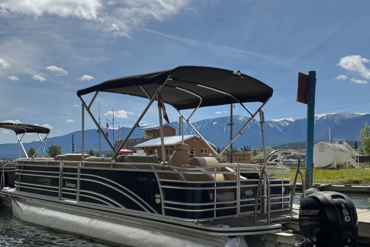 Pontoon boat docked on a sunny day with mountains in the background.