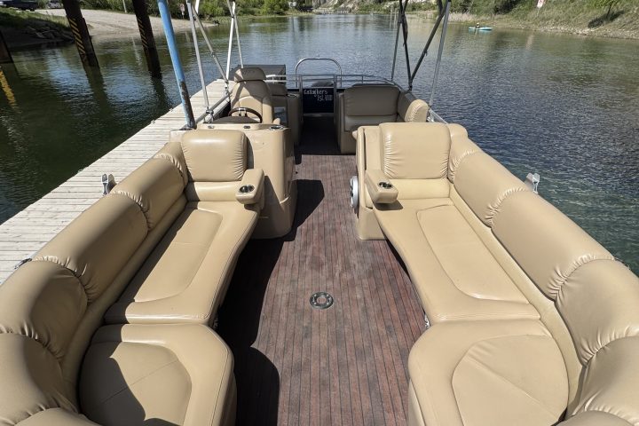 Empty pontoon boat with beige seats docked on a sunny day.