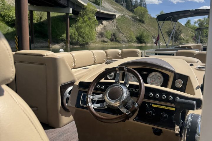 Convertible car interior with dashboard and steering wheel, parked near a bridge on a sunny day.
