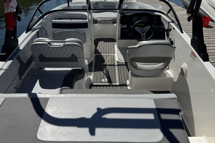 Interior of a boat with cushioned seating and a steering wheel, docked by a calm waterway.