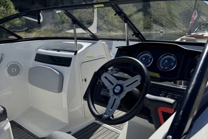 Interior of a boat with steering wheel and dashboard, sunny day.