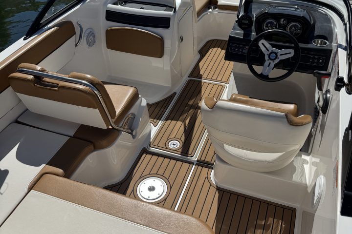 Interior of a boat with steering wheel and cream seats on a wooden deck.