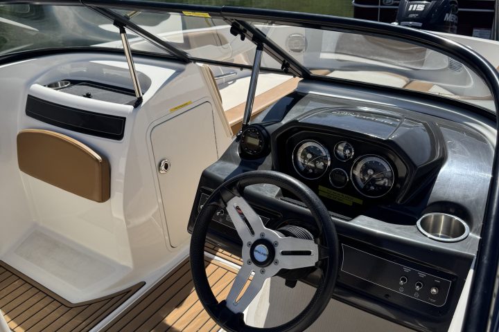 Interior view of boat cockpit with steering wheel and instrument panel.
