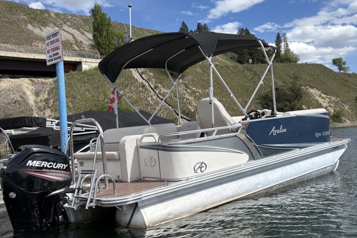 Pontoon boat docked on a lake under a blue sky with clouds.