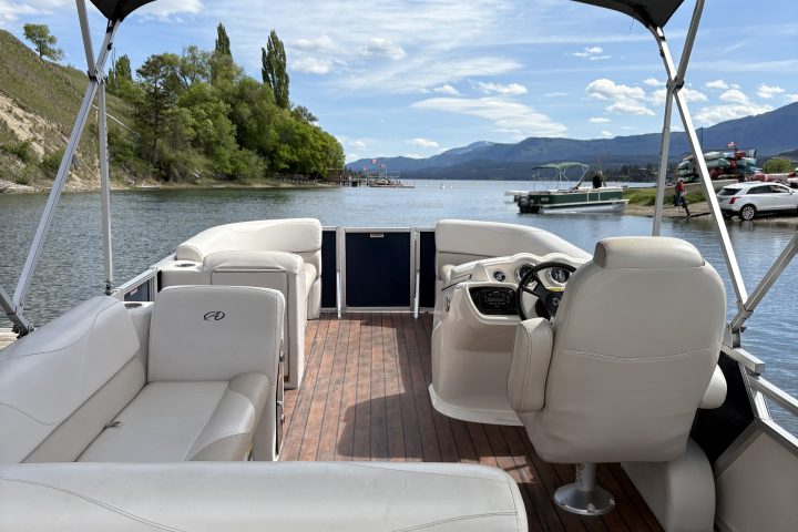 Interior of a boat with white seats and canopy, on a lake with trees and hills visible.