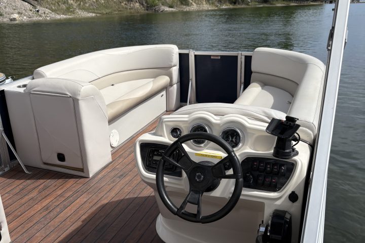Pontoon boat interior with beige seating and steering wheel on a lake.