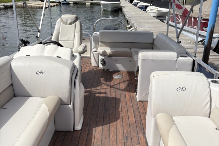 Interior of a boat with white seats and wooden deck, docked by a calm waterway.