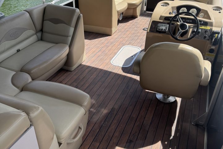 Interior of a boat with beige seats and wooden floor, near a riverbank.