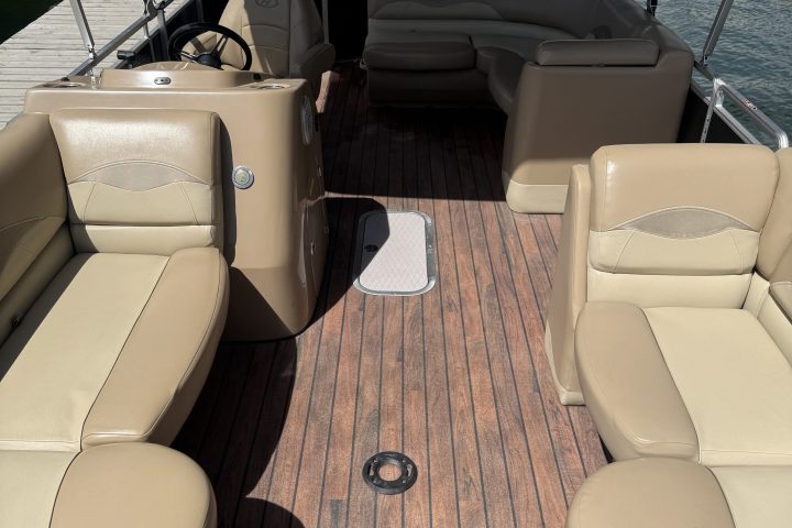 Interior of a boat with beige seats and wooden floor on a sunny day.