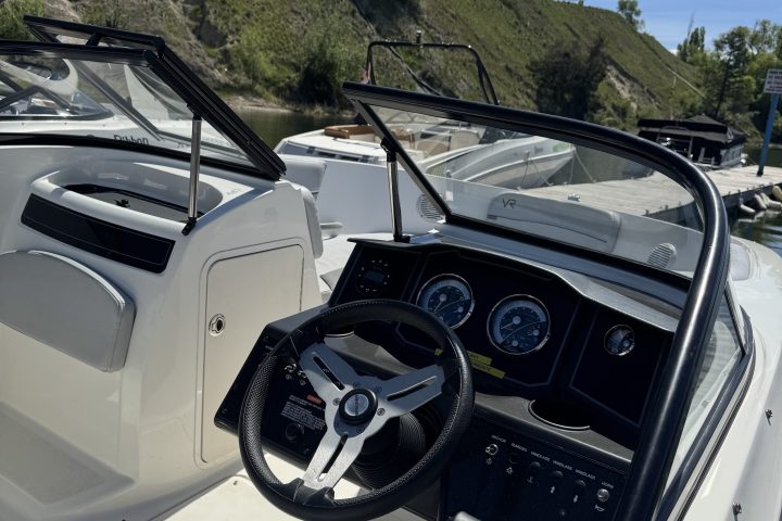 Interior of a white boat with controls, steering wheel, and open windshield.