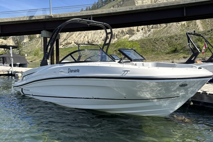 White boat docked in clear water under a bridge.